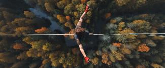 An overhead view of someone walking on a tightrope high above a forest. 