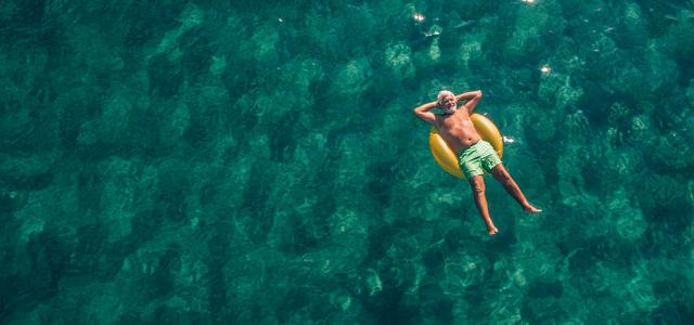 An older man relaxing and laying down in an inner tube on relaxing water.